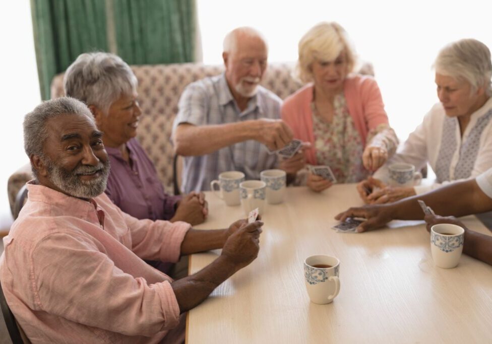 Group Of Senior People Playing Cards In Living Room